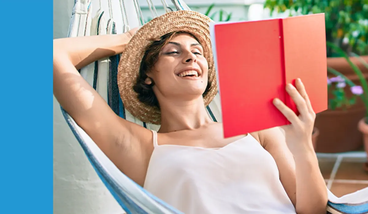 Frau liegt entspannt in der Hängematte und liest ein Buch. Grüne Pflanzen im Hintergrund vervollständigen die sommerliche Atmosphäre.